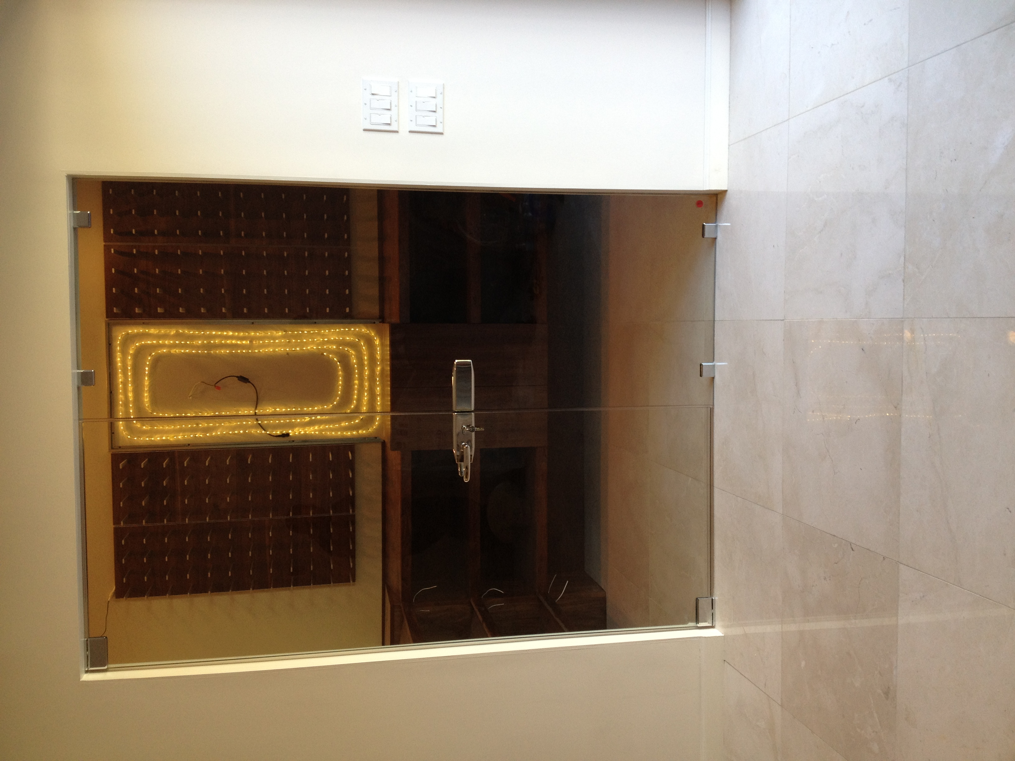 Finished wine cellar with custom glass doors, lit display racks, marble floor, luxury residential remodel by PBG.