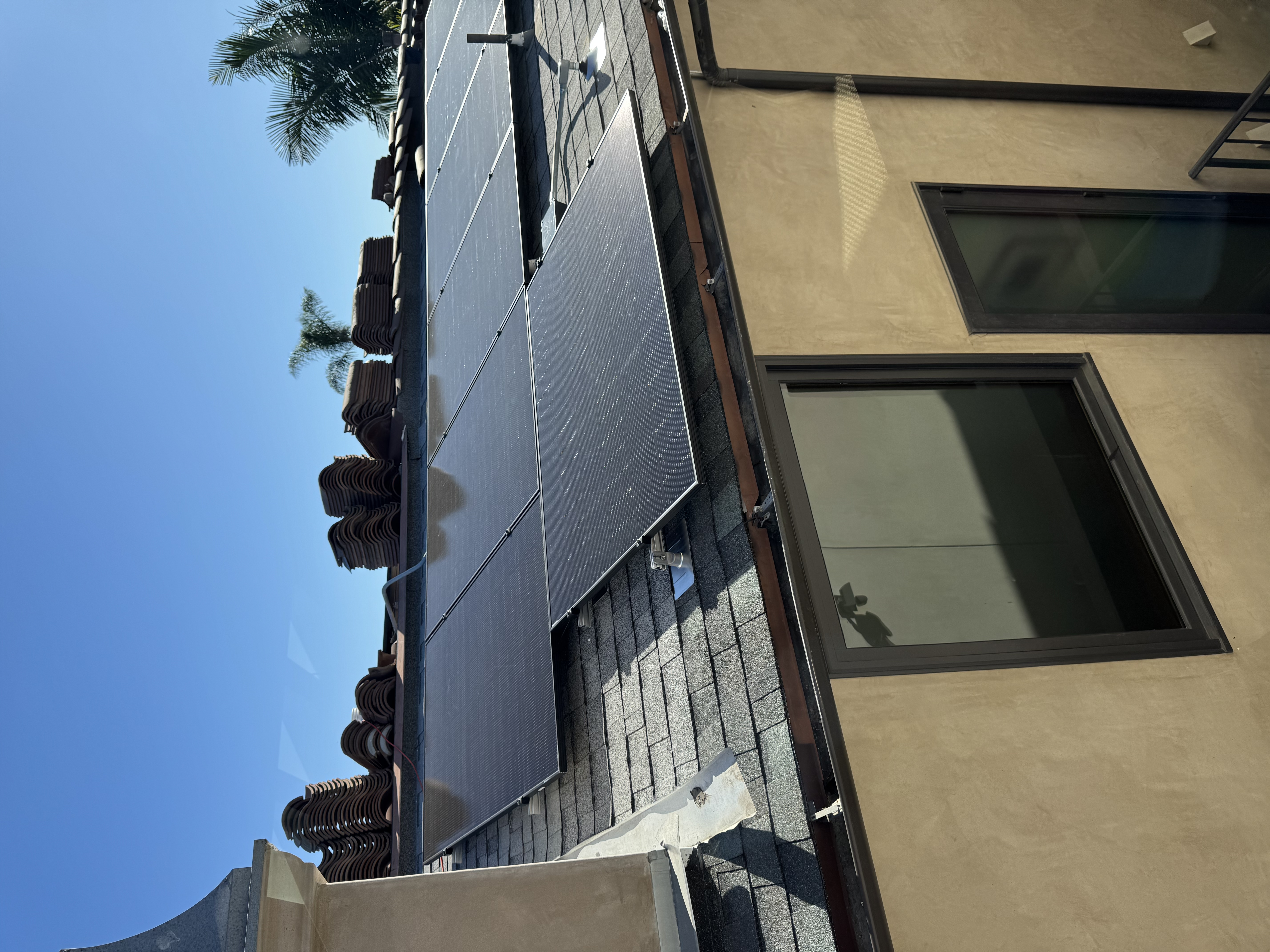 Solar panel array on Spanish-tile residential roof with palm trees, luxury residential solar & roofing by PBG.